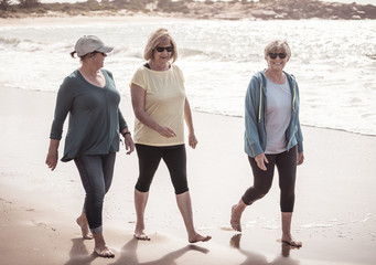Three happy senior women walking and exercising together on beach. Retirement and healthy lifestyle