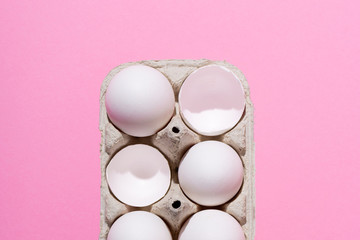 Chicken eggs in a cardboard box on a pink background. Beaten empty eggs, shell. Highlight the concept of the crowd.