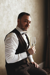 Portrait of a handsome groom with a glass of champagne in a hotel room.