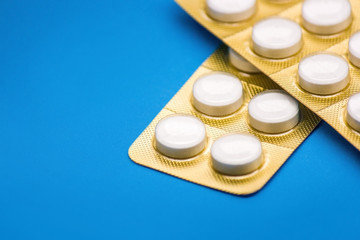 Obraz na płótnie Canvas white pills with golden blister pack on a blue background