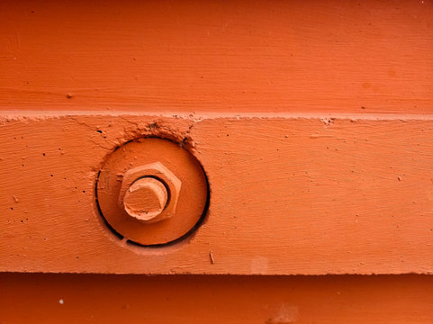 The bolt and nut are screwed into the wall of the house and painted with orange paint. The construction of a modern building. Copyspace.