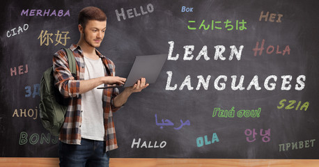 Male student wiht a laptop and standing in front of a blackboard with text learn languages