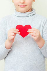 Red heart in hands of little girl on white background. Child is holding red heart.