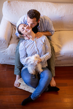 ragazzo fai i massaggi alla sua compagna che tiene in mano un cane maltese, seduto sul divano di casa mentre gli da un  bacio romantico 