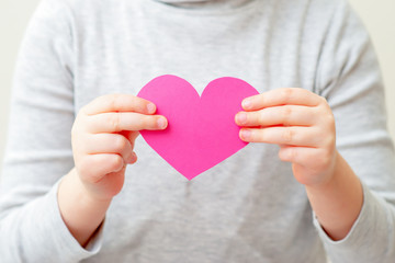 Obraz premium Child is holding pink paper heart standing on white background. Child love concept.