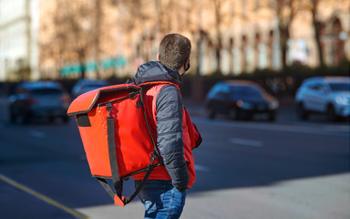 Delivery man quick delivering food from restaurant, supermarket or cafe to costumers. Delivery boy crossing road with fresh food in red backpack. Food delivery to customers home. Online food ordering