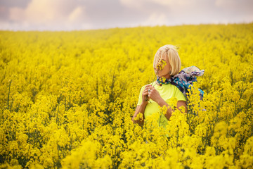 Naklejka na ściany i meble Middle-aged blonde woman among a bright yellow field of flowers.