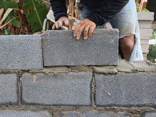 Construction workers are building cement walls with brick blocks.