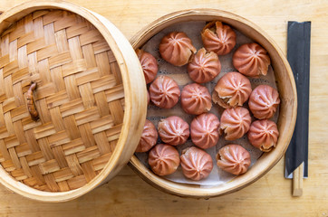 Steam basket with pink dim sum with wooden chopsticks in a case