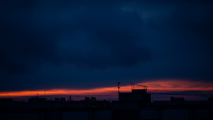 Dramatic dark sunset skyline over roofs of buildings of town.