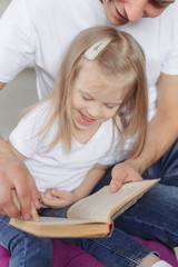 Dad teaches me how to read a little girl. The girl leads her finger on the book page.