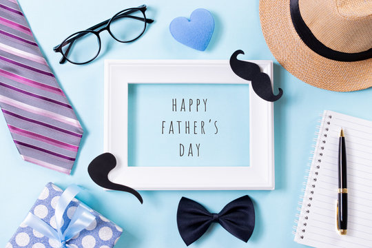 Happy fathers day concept. Top view of tie, beautiful gift box, hat, white picture frame with Happy father's day text on bright blue pastel background. Flat lay.