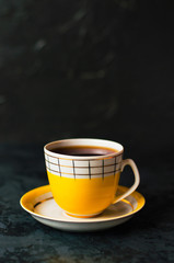Yellow cup with coffee without foam on a dark background, vertical photo format