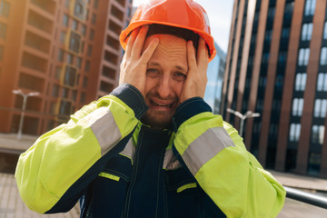 Spastel young man in a helmet close-up, upset in shock, holding his head. The concept of saving people's lives