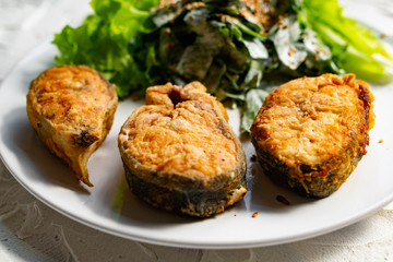 Colorful delicious dish with a salad of sorrel and sour cream, topped with fried sesame seeds, next to fried steaks of red fish pink salmon in breadcrumbs