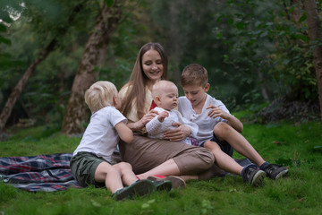 Naklejka na ściany i meble Young mother with little children having picnic in summer. Happy family sitting on meadow