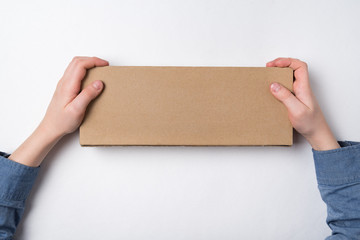 Child holds rectangular craft paper box on white background. Parcel delivery concept. Top view. Copy space.