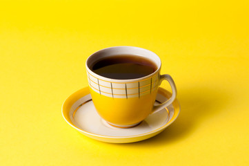 Yellow cup of tea or coffee on a yellow background. Minimalistic composition with a vintage subject and place for text.