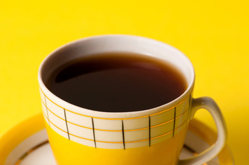 Yellow cup of tea or coffee without foam, close-up on a yellow background. Minimalistic composition with vintage subject and place for text.
