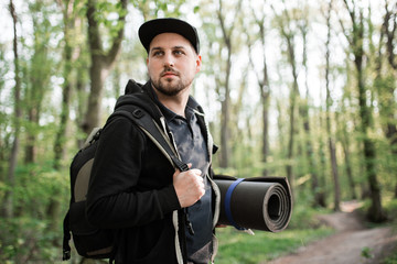 Young man traveler walking in forest with bagpack