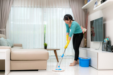 Attractive young Asian woman mopping tile floor at living room while doing cleaning at home during Staying at home using free time about their daily housekeeping routine..