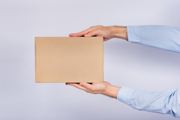 Man holding box at arm's length. Cardboard box. Delivery of parcels. Side view.