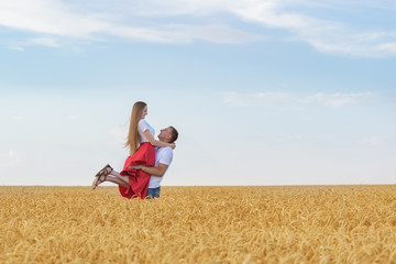 Happy young couple have fun in wheat field on sunny summer day. A man holds beloved in his hands