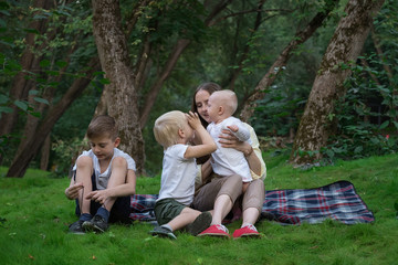 Naklejka na ściany i meble Happy family of four having picnic at the park. Mother and three children sitting on picnic blanket. Weekend outdoors
