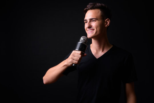 Portrait of happy young handsome man thinking while using microphone