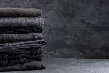 A stack of neatly folded dark clothes isolated on a black gray background close-up - obrazy, fototapety, plakaty