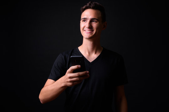 Portrait of happy young handsome man thinking while using phone
