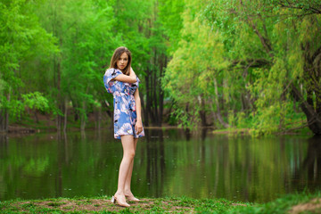 Portrait of a young beautiful woman in blue dress posing by the lake