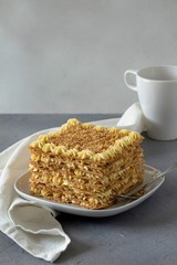Napoleon cake on a white plate with a linen napkin on a gray background and a white cup. Copy space.