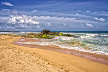 Sandy beach with mossy rocks in water.