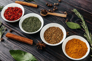 Flat displays of various spices in small white plates on a rustic wooden table.