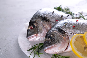 Fresh raw sea bream fish decorated with lemon slices, herbs on gray background. Healthy food concept, top view, copy space