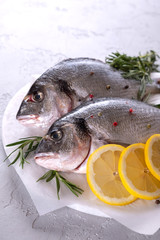 Fresh raw sea bream fish decorated with lemon slices, herbs on gray background. Healthy food concept, top view, copy space