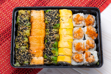 Set of rolls sushi with salmon and vegetables in black tray on red wicker dining mat. A Japanese dish of seafood.