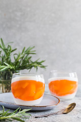 homemade panna cotta with slices of peach and peach jelly in glass jars on a gray concrete background