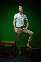 Handsome young man in stylish clothes posing against green studio background 