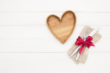 Place Setting. Empty wooden  plate, fork and knife on white  background.Wooden plate heart shape.Love food, love eating, romantic dinner , Valentine's day
