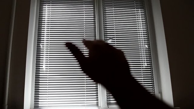 Close-up unfocused silhouette of a man's hand reaching for the light against the background of a window in the room. Hand silhouette raised up to the light.