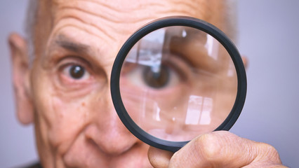 older man looking through magnifying glass closeup
