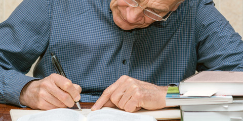 old elderly man writing with pen in rihgt hand books pile on table knowledge concept