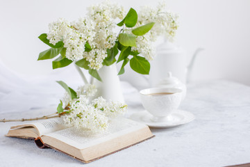 Fototapeta na wymiar Still life vase with a bouquet of white lilac, a Cup of coffee ,, a sugar bowl and a milk jug , an old book. Postcard good morning.