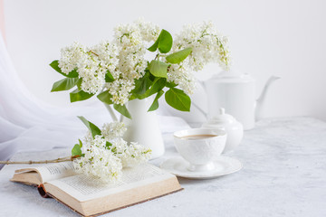 Still life vase with a bouquet of white lilac, a Cup of coffee with marshmallows, a plate of meringue, a sugar bowl and a milk jug , an old book. Postcard good morning.