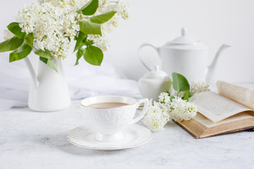 Still life vase with a bouquet of white lilac, a Cup of coffee with marshmallows, a plate of meringue, a sugar bowl and a milk jug , an old book. Postcard good morning.