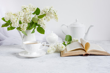 Still life vase with a bouquet of white lilac, a Cup of coffee with marshmallows, a plate of meringue, a sugar bowl and a milk jug , an old book. Postcard good morning.