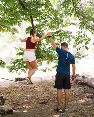 Young people doing Slacklining is a practice in balance that typically uses nylon or polyester webbing tensioned between two anchor points. - 346565797