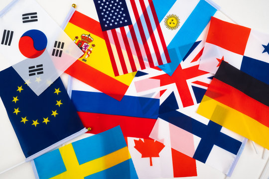 National flags are on a white table. Political and economic relations of States. International cooperation. Union of States. Associations of countries. State symbols of different countries together.